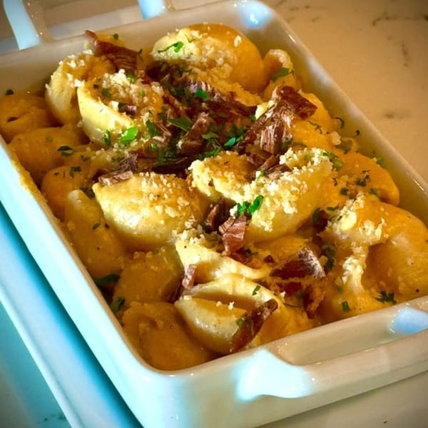 Vegan mac and cheese with shell pasta, topped with crumbled vegan bacon and fresh parsley.