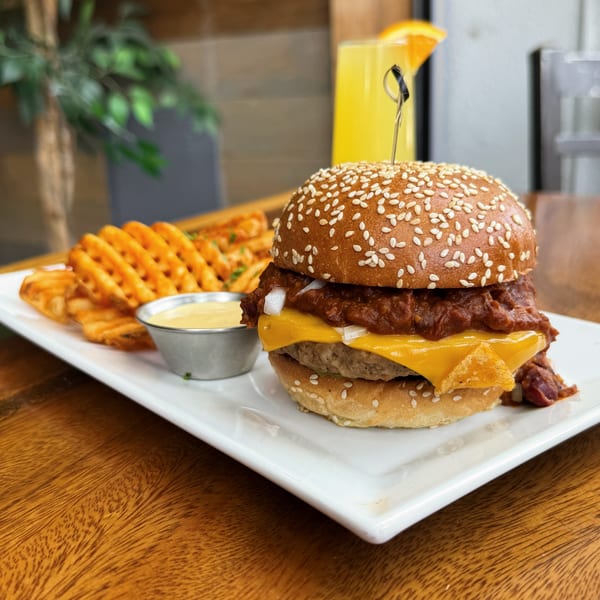 Ocado Restaurant's vegan chili cheeseburger with waffle fries and dipping sauce, next to an orange juice.