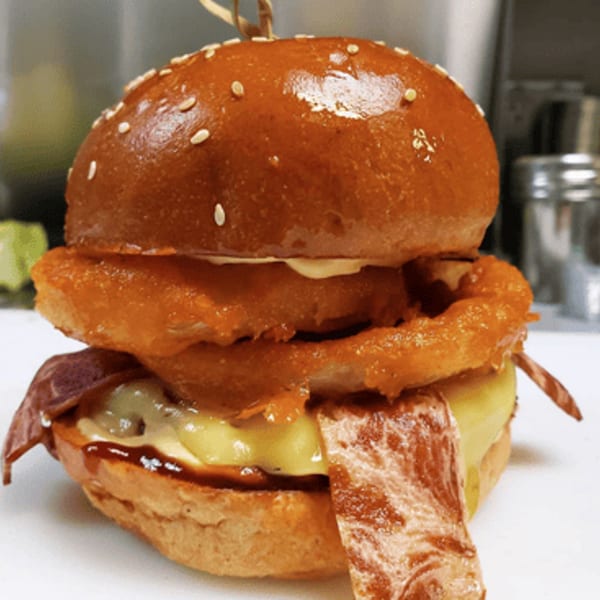 Ocado Restaurant's vegan burger with onion rings, cheese, and bacon on a sesame seed bun.