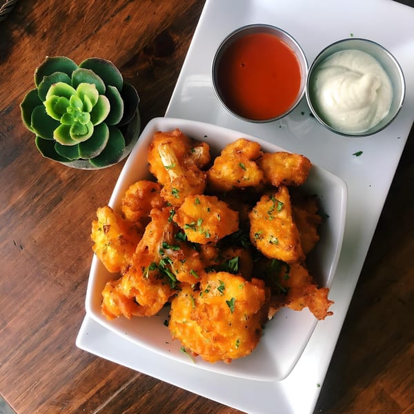 Vegan fried cauliflower bites with two dipping sauces and a succulent on a wooden table.