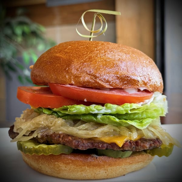 A vegan burger with a patty, cheese, caramelized onions, pickles, lettuce, tomatoes, and sauce.