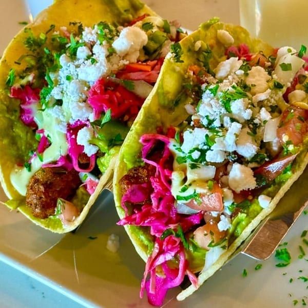 Two vibrant vegan tacos with falafel, guacamole, pickled cabbage, and crumbled cheese on a white plate.