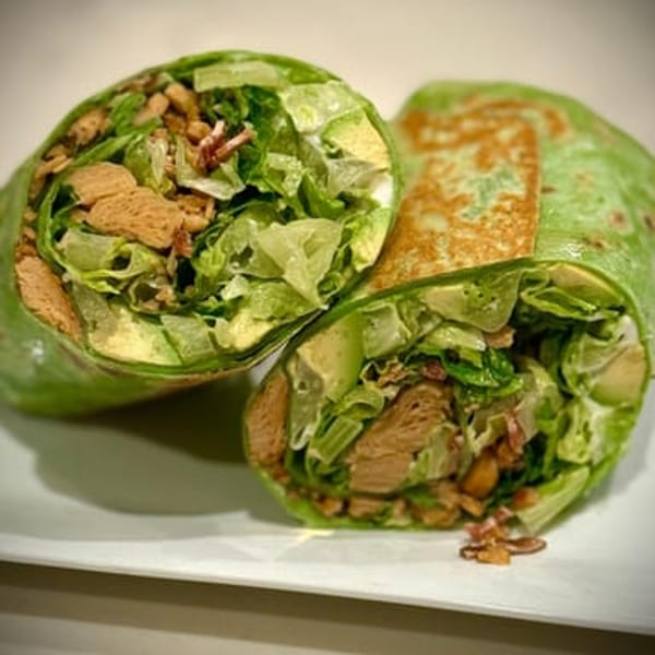 Two halves of a vegan wrap, filled with lettuce, avocado, and crispy brown pieces.
