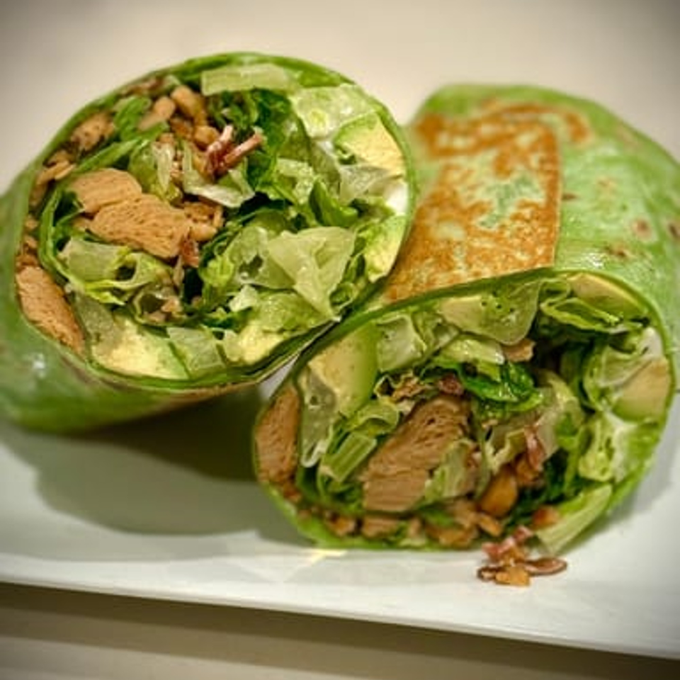 Two halves of a vegan wrap, filled with lettuce, avocado, and crispy brown pieces.