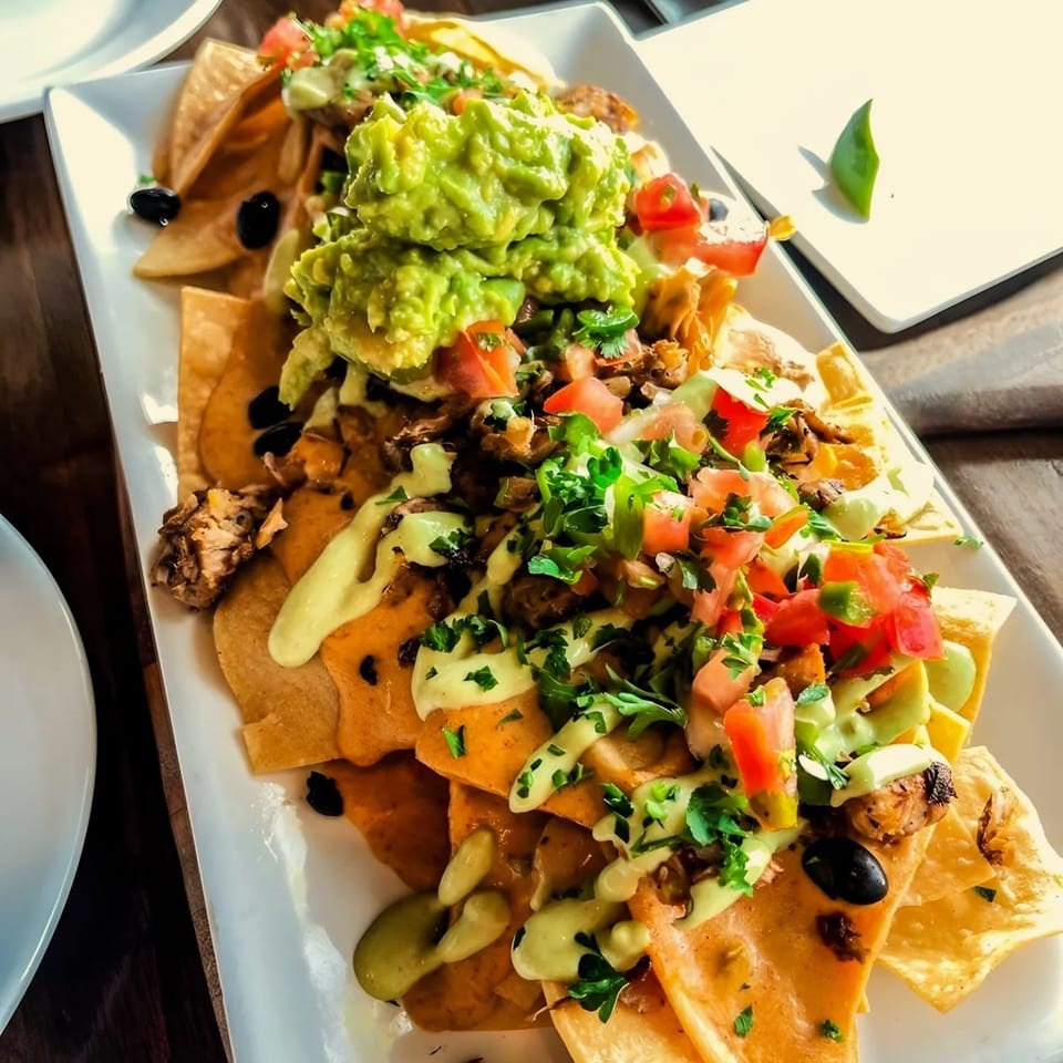 Ocado Restaurant's vegan nachos, topped with guacamole, salsa, black beans, and a creamy sauce.